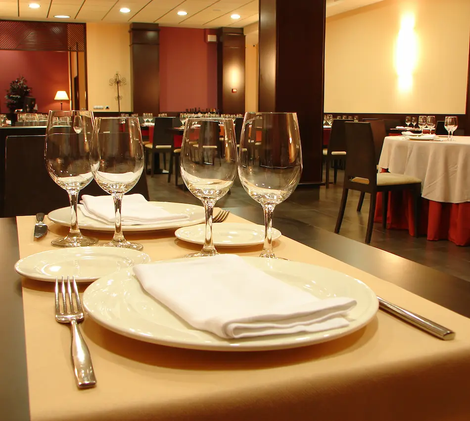 Mesa de restaurante elegante con copas, platos y servilletas blancas. Ambiente sofisticado.