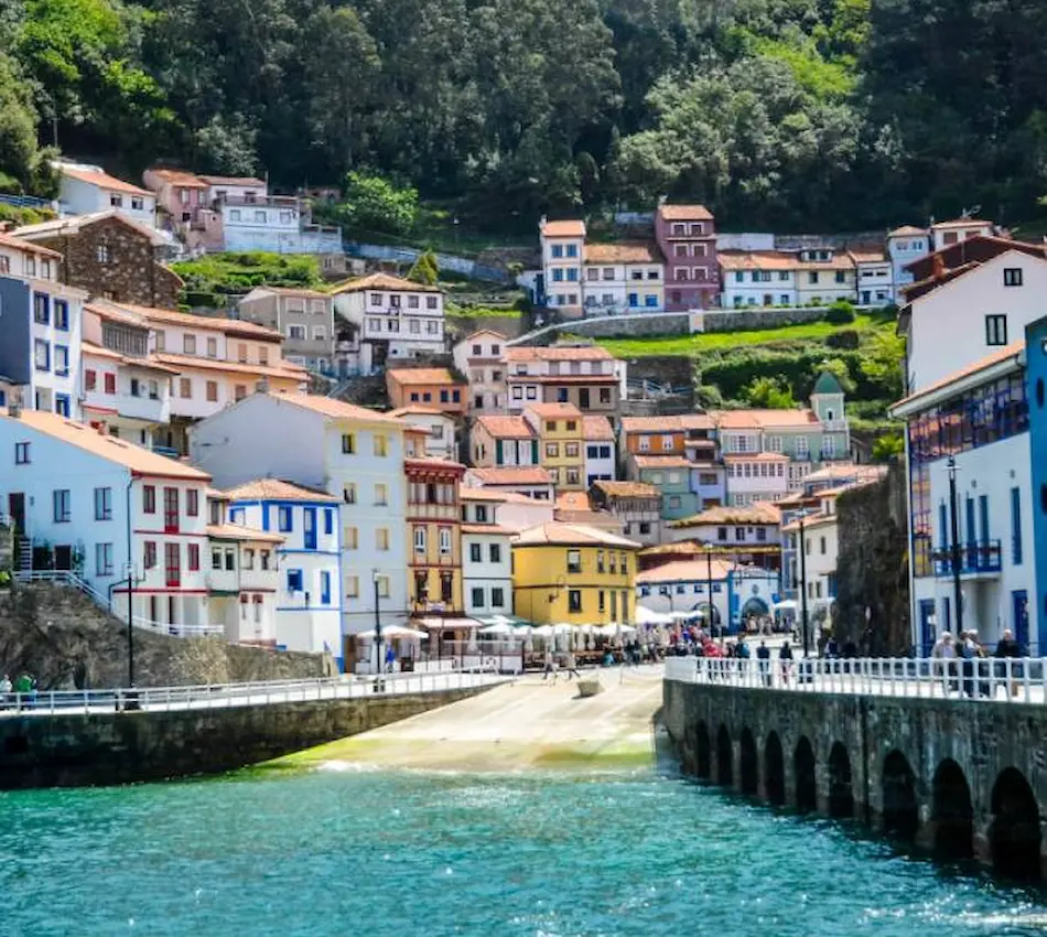 Casas coloridas en una colina junto al mar, con un muelle y vegetación exuberante.
