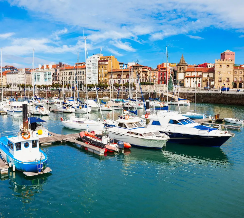 Puerto deportivo con barcos y edificios coloridos al fondo bajo un cielo azul.