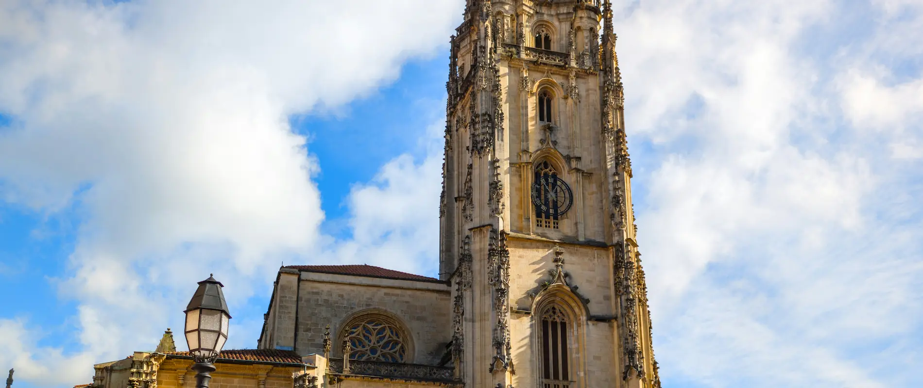 Torre de iglesia gótica bajo un cielo azul con nubes blancas.