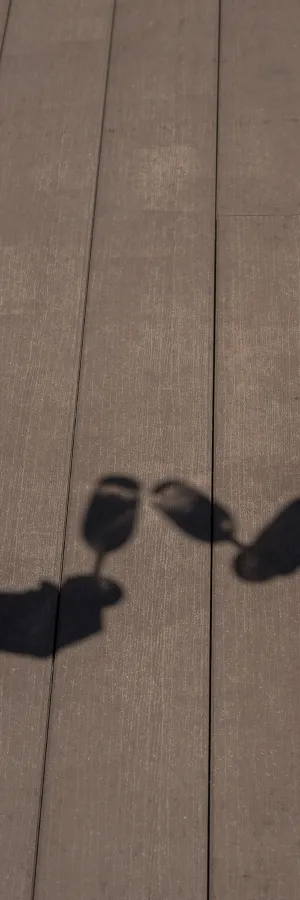 Sombras de dos copas brindando sobre una plataforma de madera.