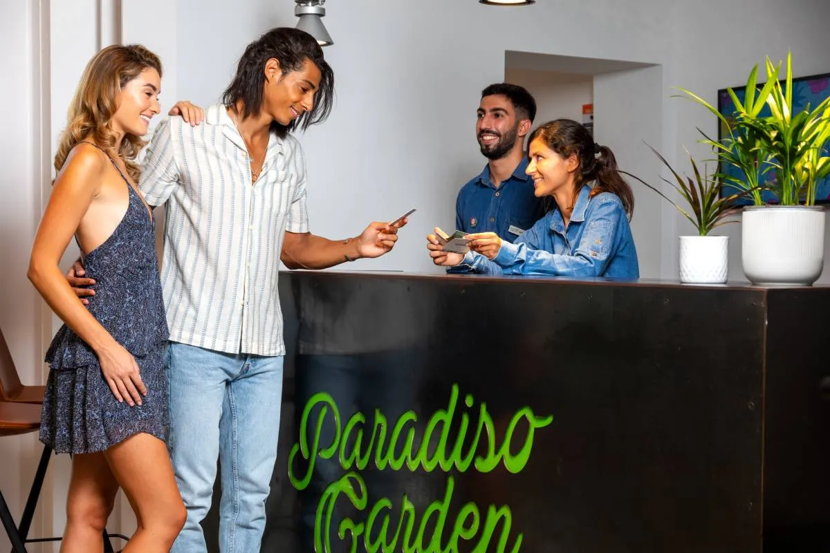 Pareja en una recepción de hotel, atendida por dos empleados sonrientes detrás del mostrador.