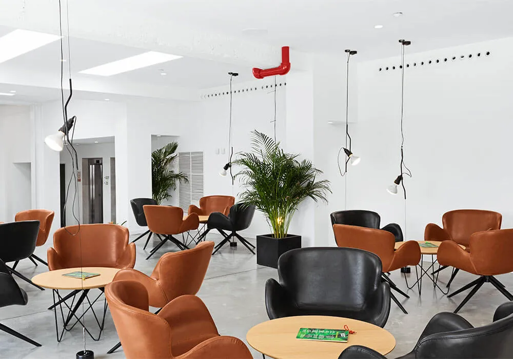 Sala moderna con sillas de cuero, mesas, plantas y lámparas colgantes. Ambiente luminoso.