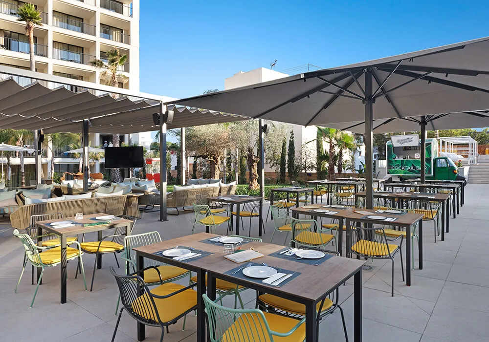 Terraza al aire libre con mesas, sillas amarillas y sombrillas grandes.
