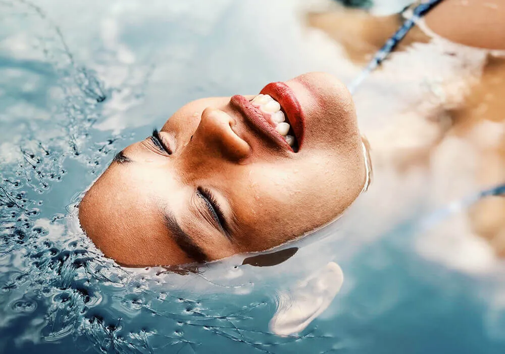 Persona flotando con ojos cerrados y sonrisa en el agua de una piscina.
