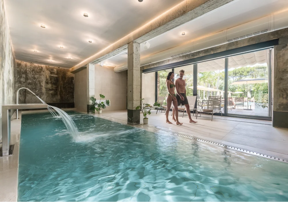 Piscina interior moderna con dos personas en traje de baño caminando.