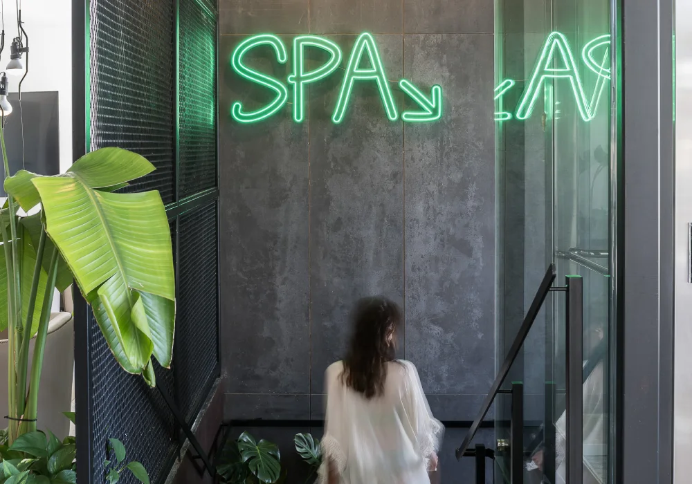 Persona descendiendo escalera hacia un spa con letrero de neón verde.