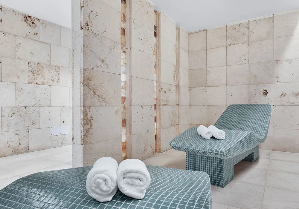 Espacio de spa con dos camillas revestidas de mosaico verde y toallas blancas enrolladas encima.