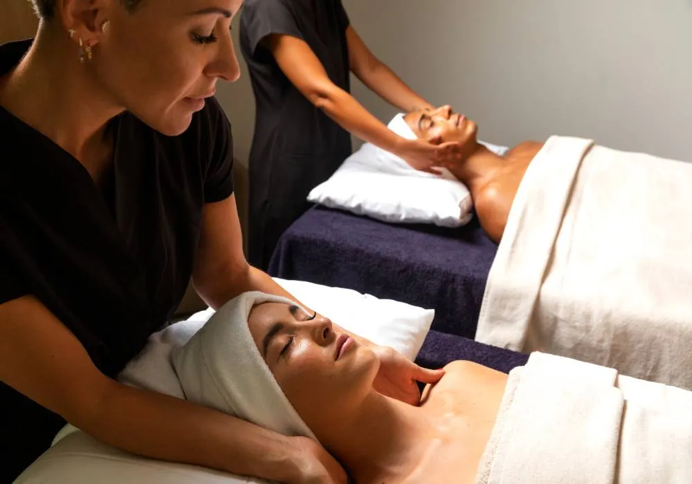 Personas recibiendo masajes faciales en un spa, cubiertas con mantas blancas.