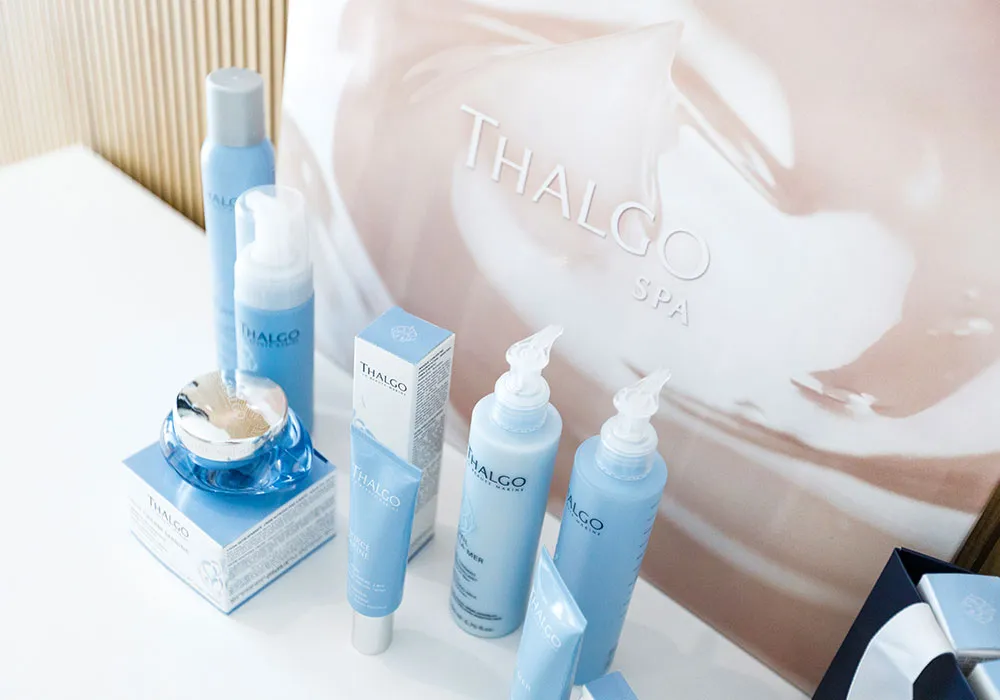 Productos de belleza Thalgo en envases azules sobre una mesa blanca.