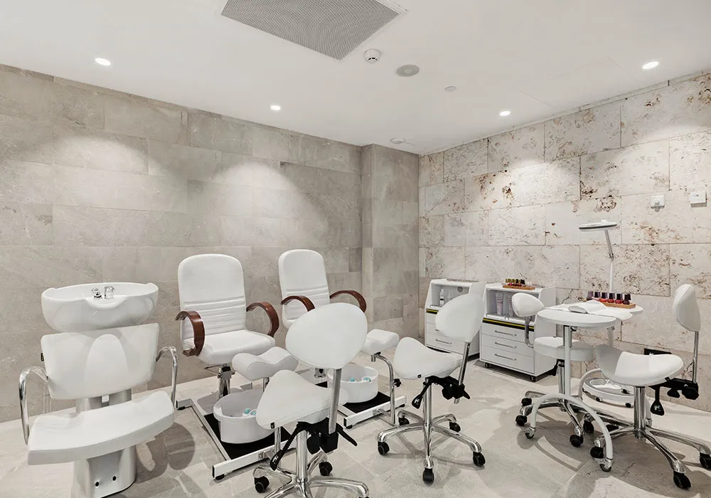 Sala de manicura y pedicura con sillas blancas, lavamanos y mesas para tratamientos.