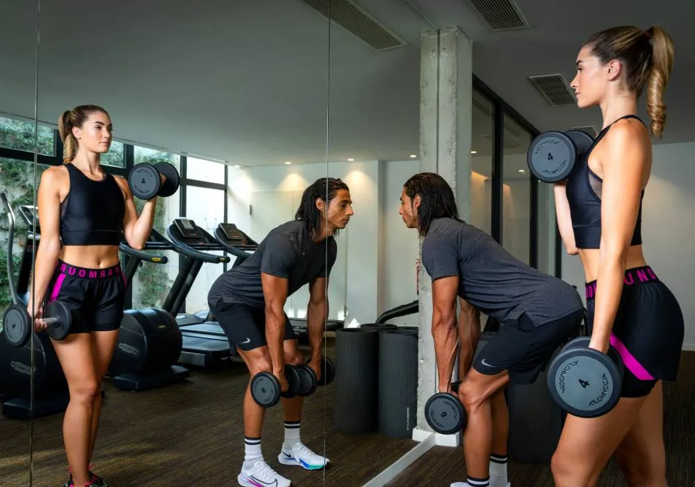 Personas levantando pesas frente a un espejo en un gimnasio moderno.