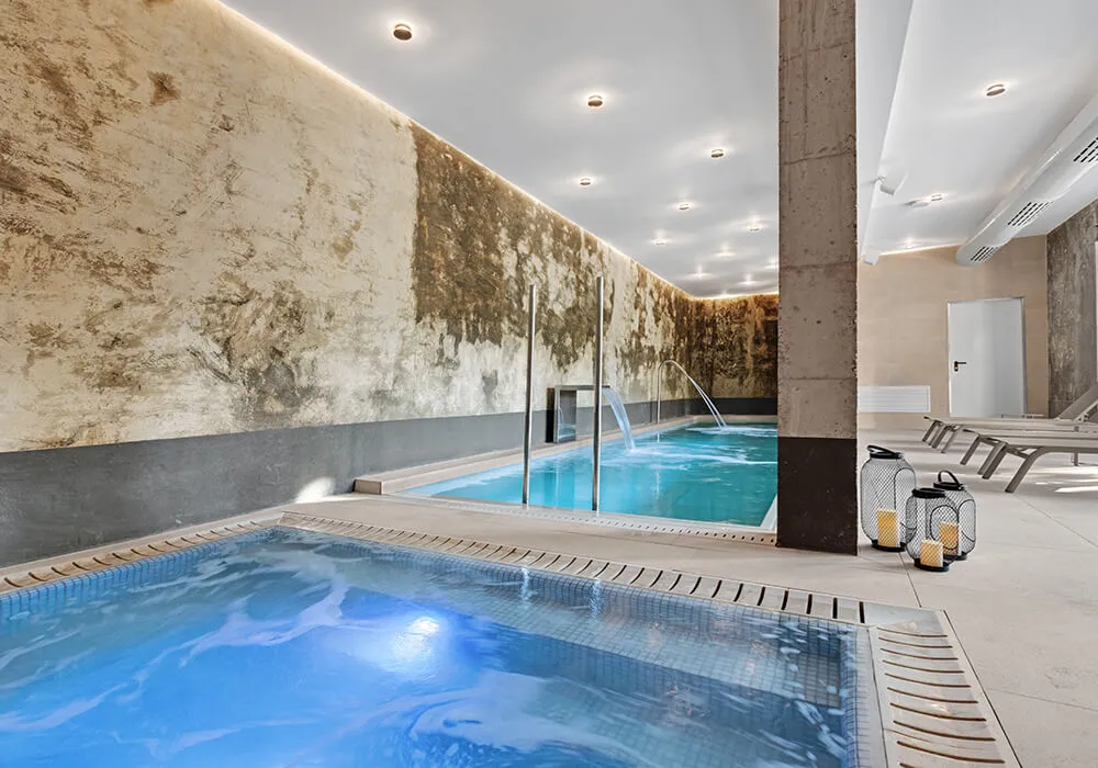Piscina interior moderna con iluminación suave, velas decorativas y tumbonas a un lado.