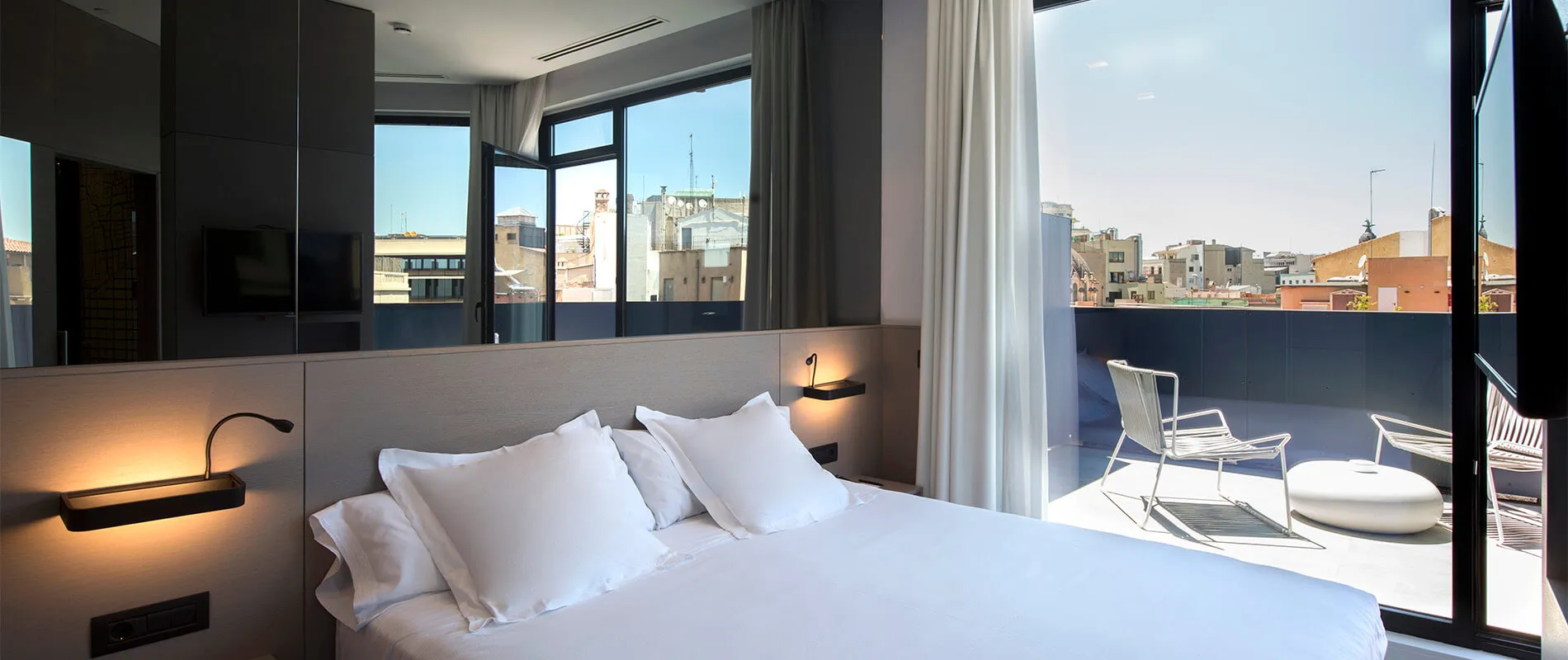 Habitación de hotel moderna con cama doble y terraza con vista a edificios urbanos.