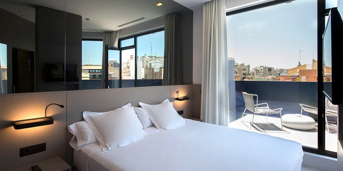 Habitación moderna con cama doble y terraza, vista a la ciudad y gran entrada de luz natural.