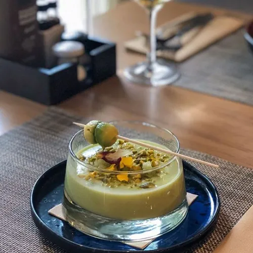 Postre en vaso con decoraci&oacute;n floral y brocheta, sobre un plato azul en un restaurante.