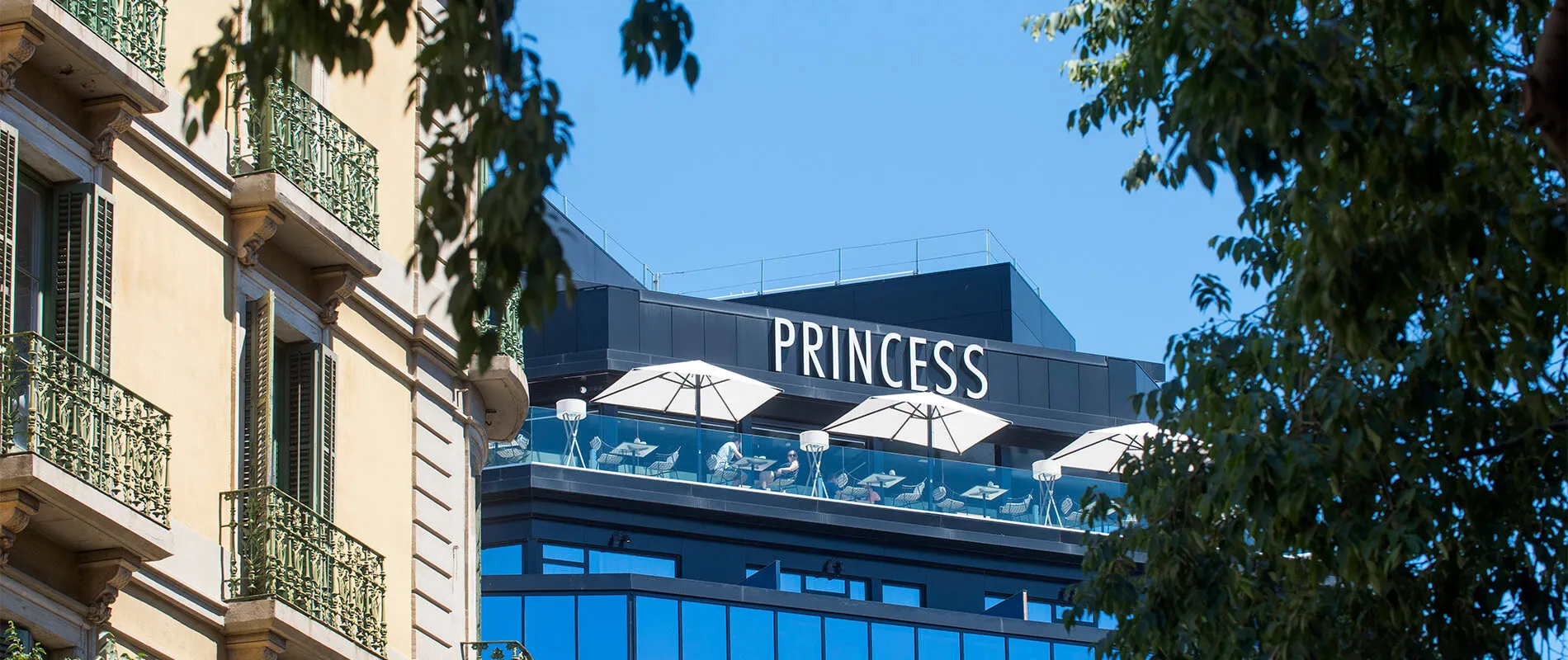 Edificio moderno con terraza y letrero "Princess", junto a otra edificación con balcones clásicos.