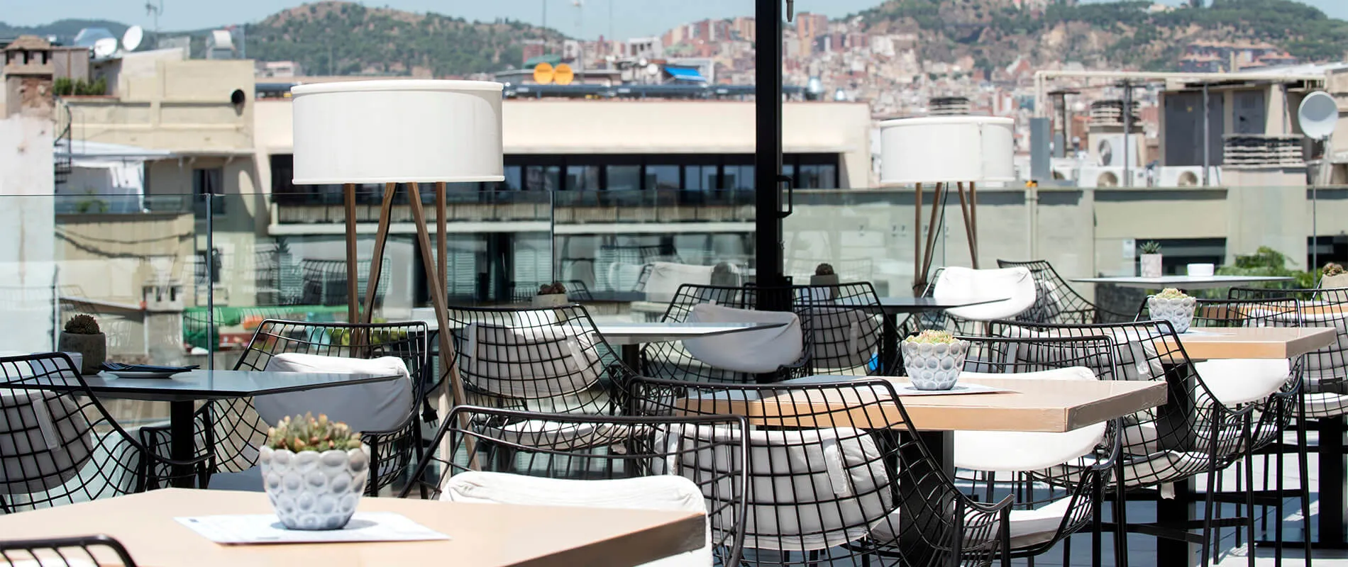 Terraza con mesas y sillas de diseño moderno, decorada con plantas y lámparas, vista a la ciudad.