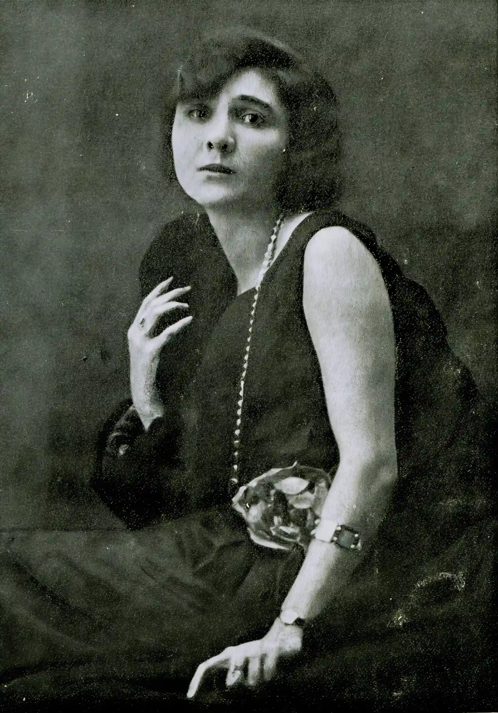 Black and white portrait of a woman in a dress, looking at the camera, with a pearl necklace.