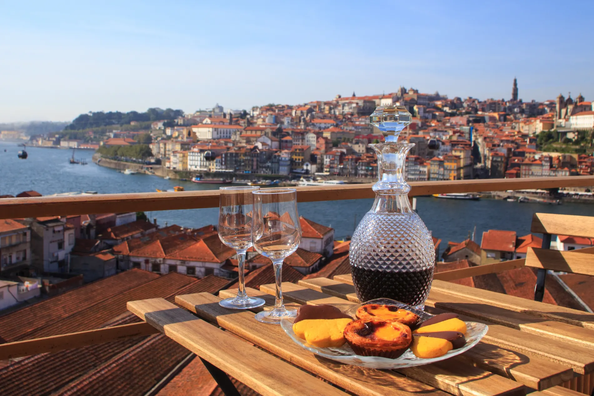Wine and pastries on a table overlooking a river and cityscape with red-roofed buildings.