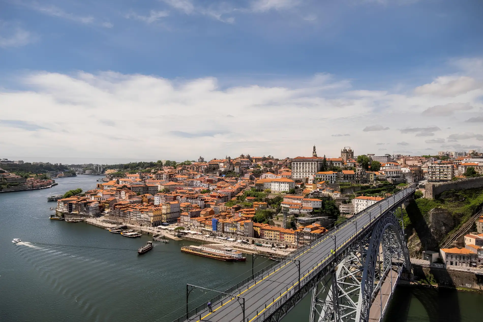 A scenic view of a city with a bridge over a river, featuring historic buildings and a cloudy sky.
