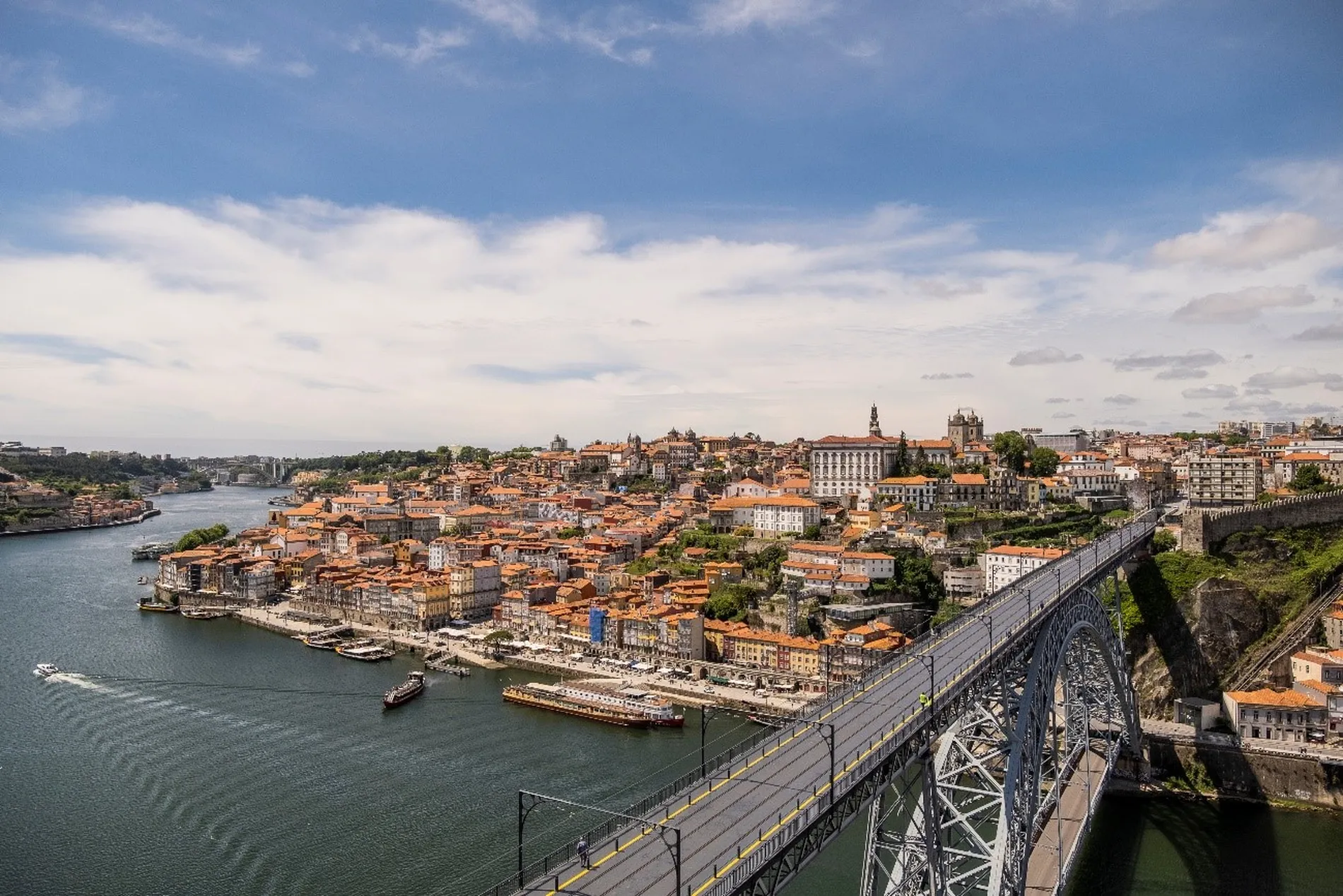 Cityscape of Porto, Portugal with Douro River and Dom Luís I Bridge under a partly cloudy sky.