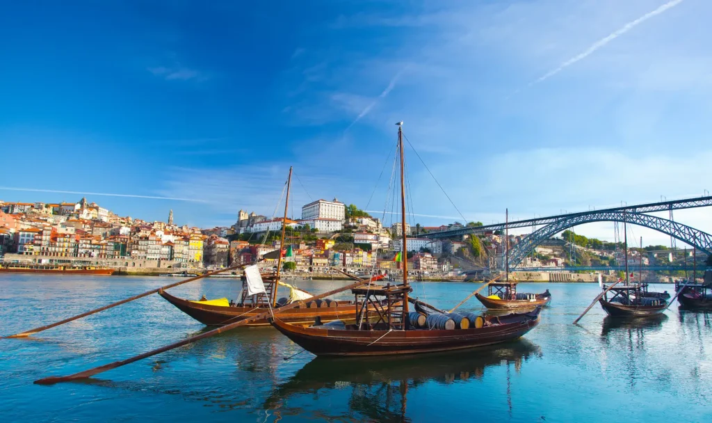 Boats on a river with a city and bridge in the background under a clear blue sky.