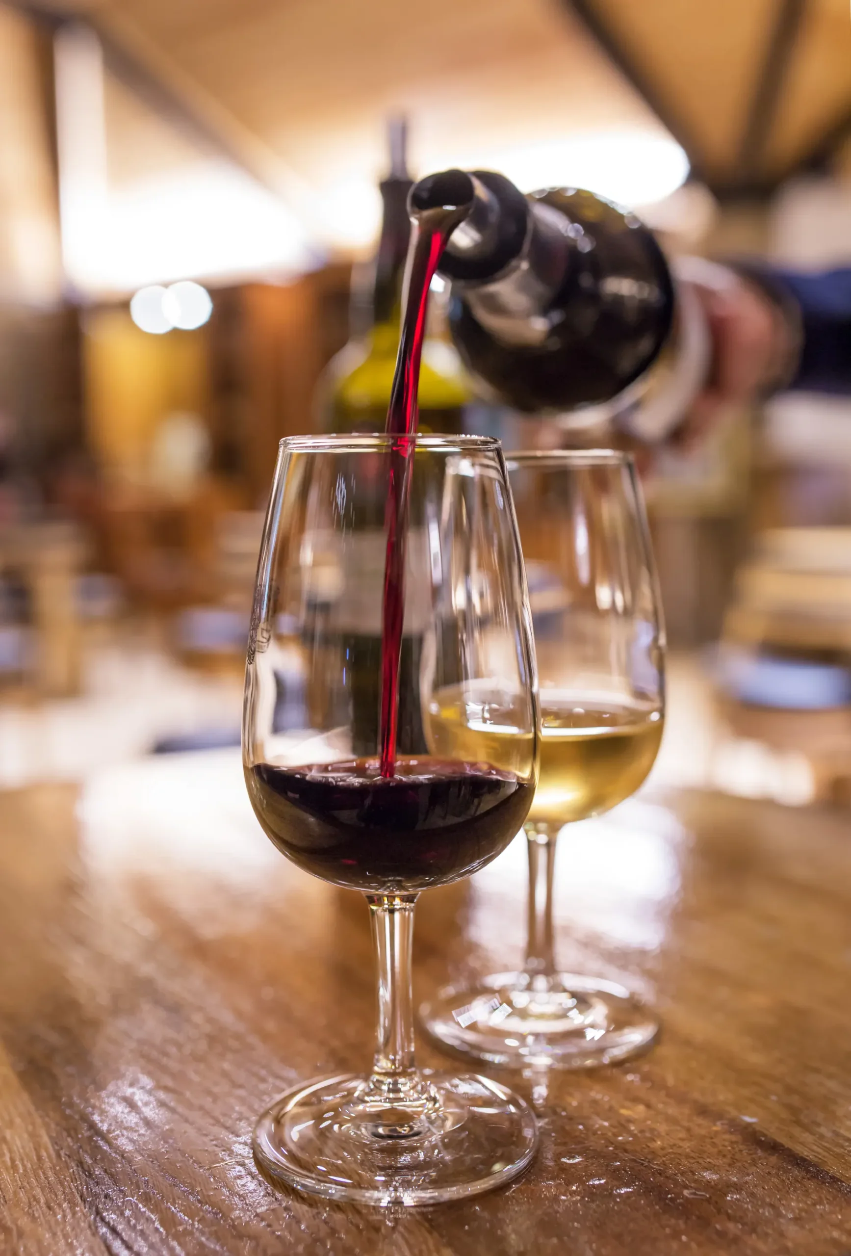 Red wine being poured into a glass next to a filled white wine glass on a wooden table.