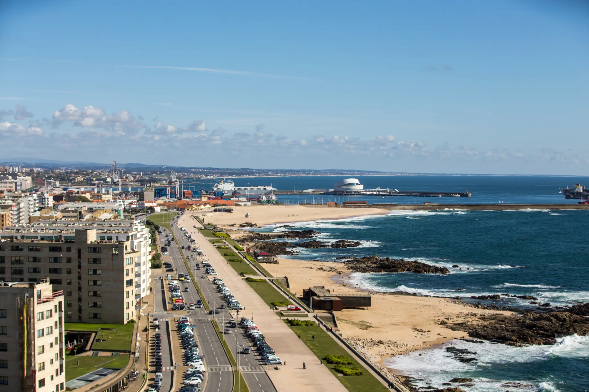 Coastal cityscape with beaches, buildings, and a harbor under a clear blue sky.