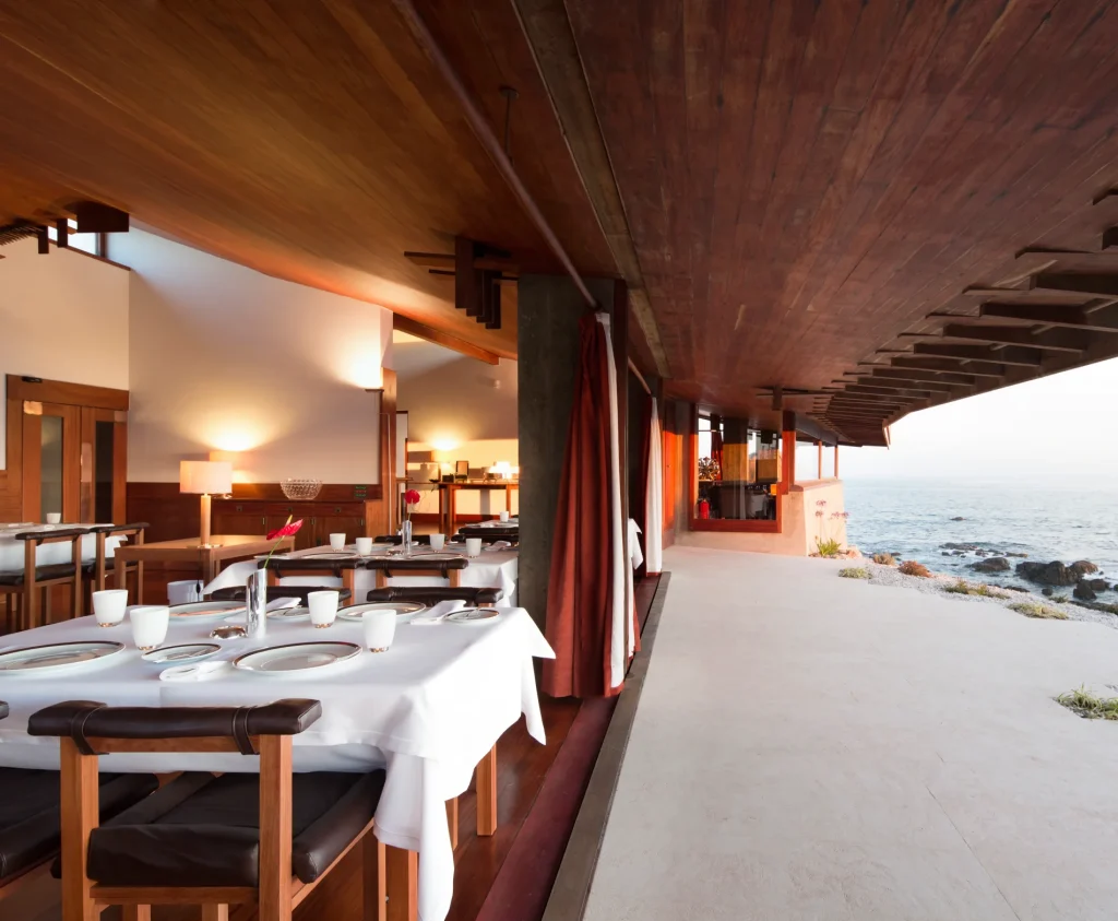 Dining area beside a sea view with wooden ceiling and set tables.