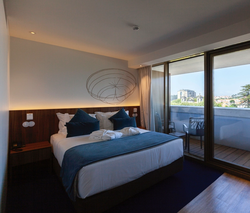 Modern hotel room with a king-size bed, balcony view, and stylish decor.
