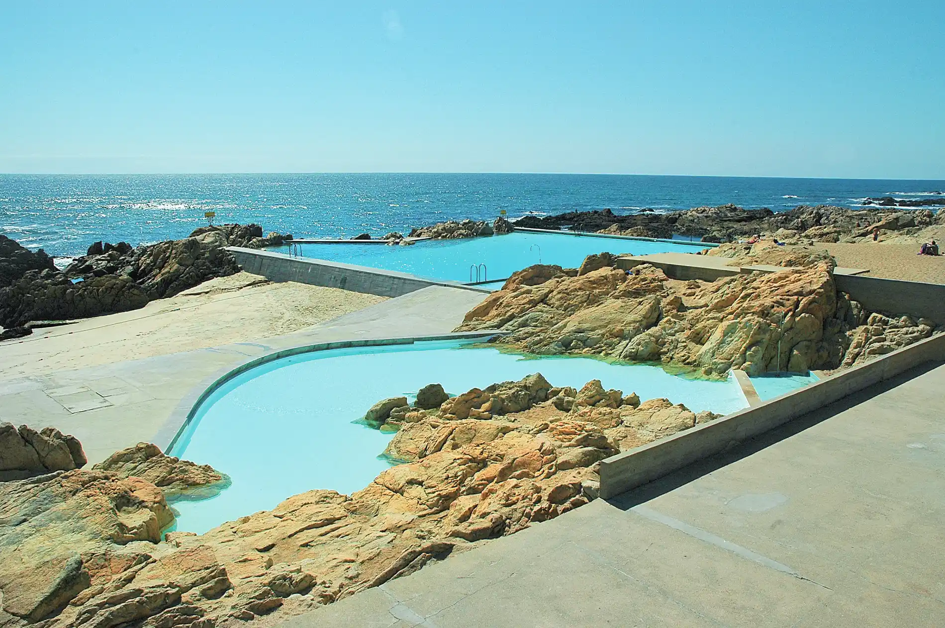 Oceanfront pool with rocky landscape and clear blue sky.