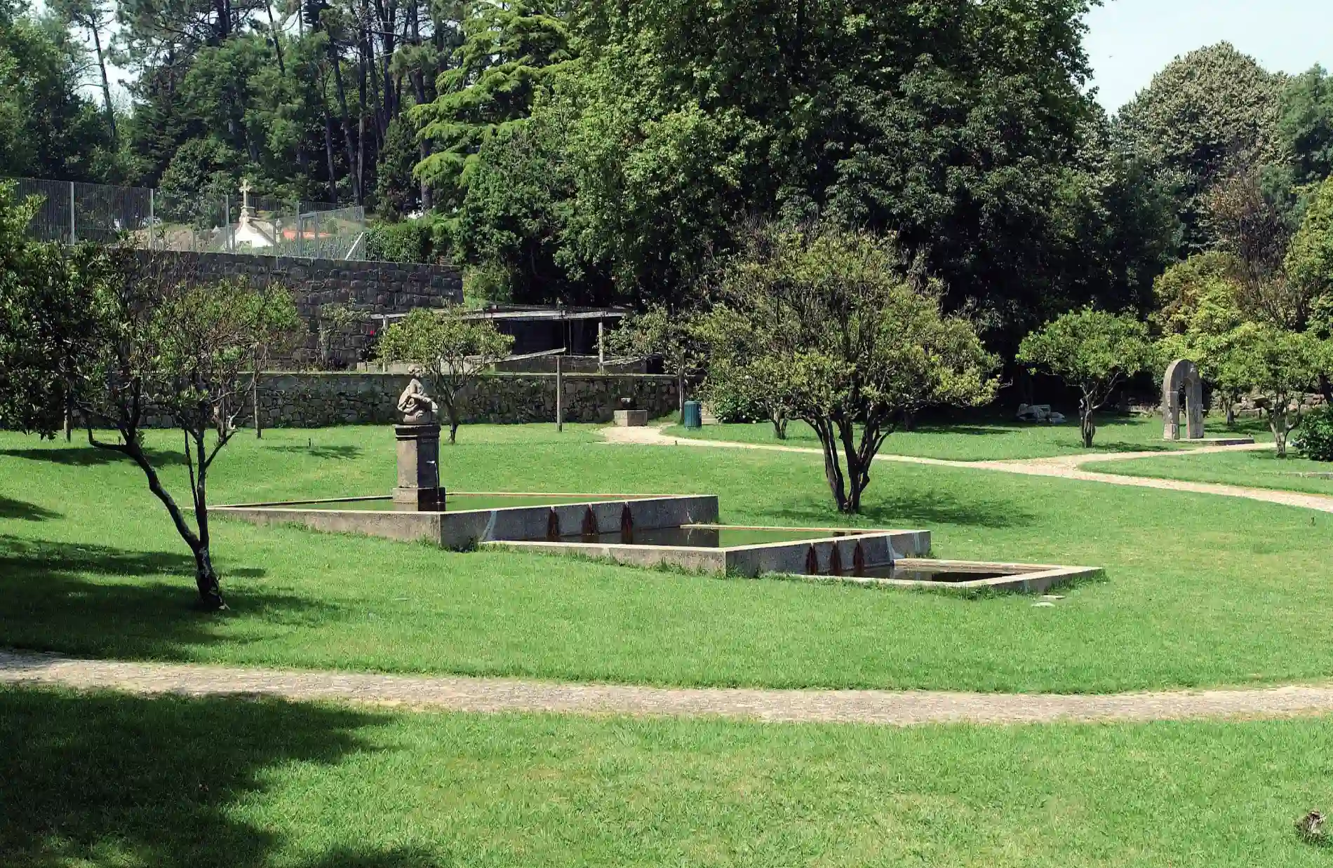 Park landscape with green grass, trees, pathways, and a small statue.