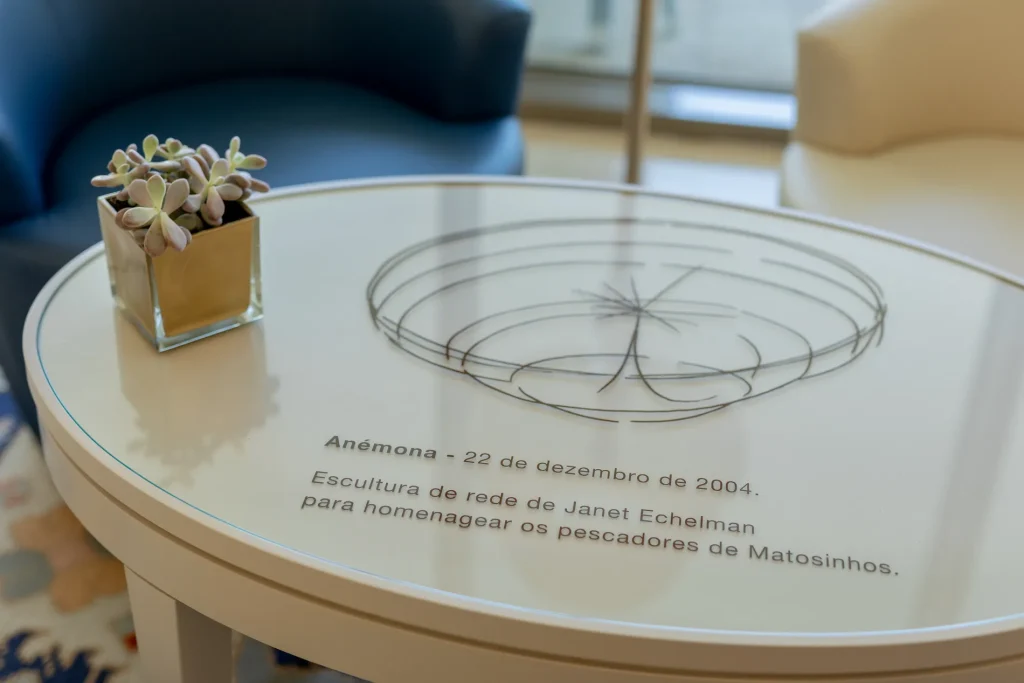 A table with a small plant and text about Janet Echelman's sculpture honoring Matosinhos fishermen.