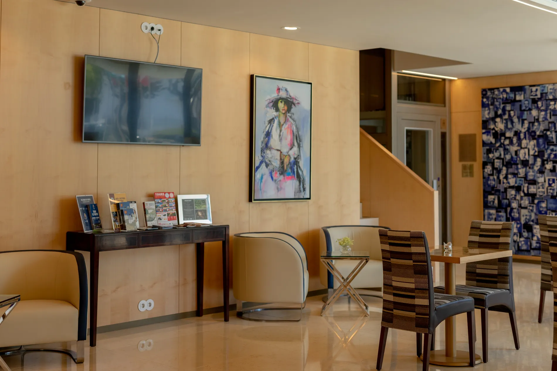 Lobby with chairs, a table, a wall-mounted TV, and a colorful painting. Brochures on a desk.
