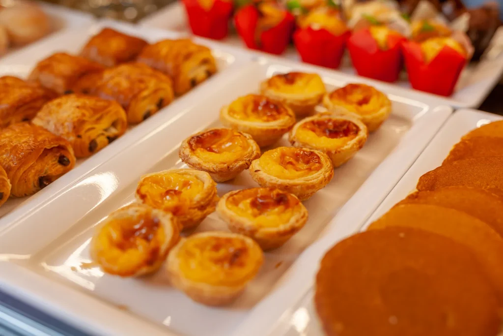 Assorted pastries on white trays, including custard tarts and rolls.