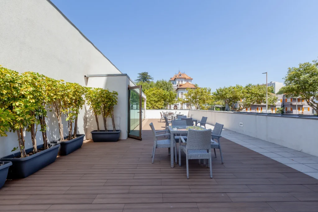 Rooftop terrace with tables, chairs, and potted plants under a clear blue sky.
