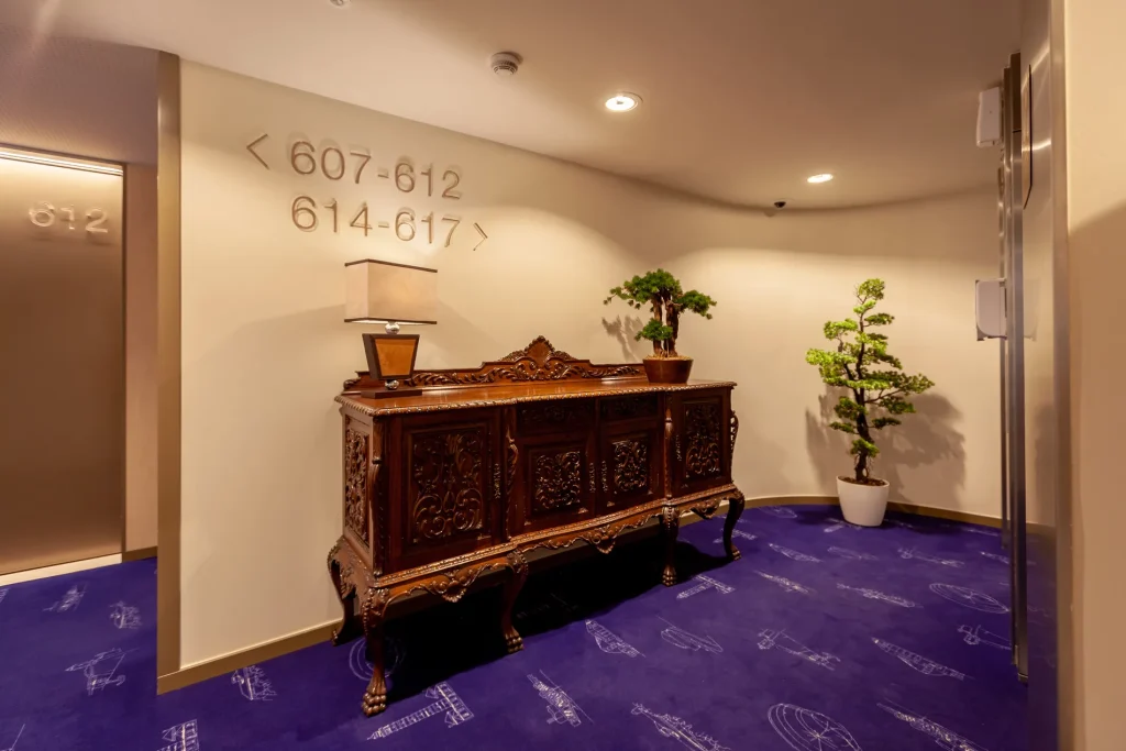 Hallway with carved sideboard, potted plants, and directional room numbers on the wall.