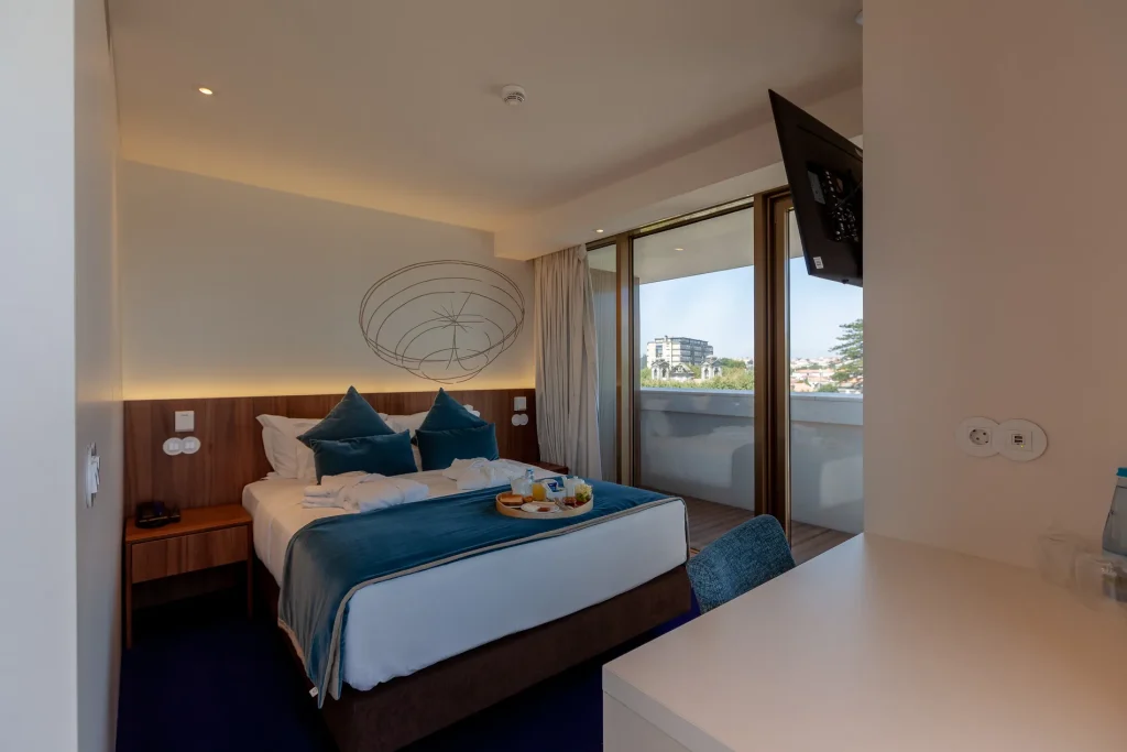 Cozy modern hotel room with a large bed, balcony view, wall art, and breakfast tray.