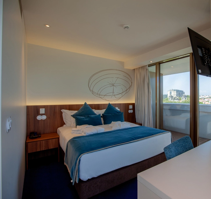 Modern hotel room with a blue-accented bed and a city view through large glass doors.