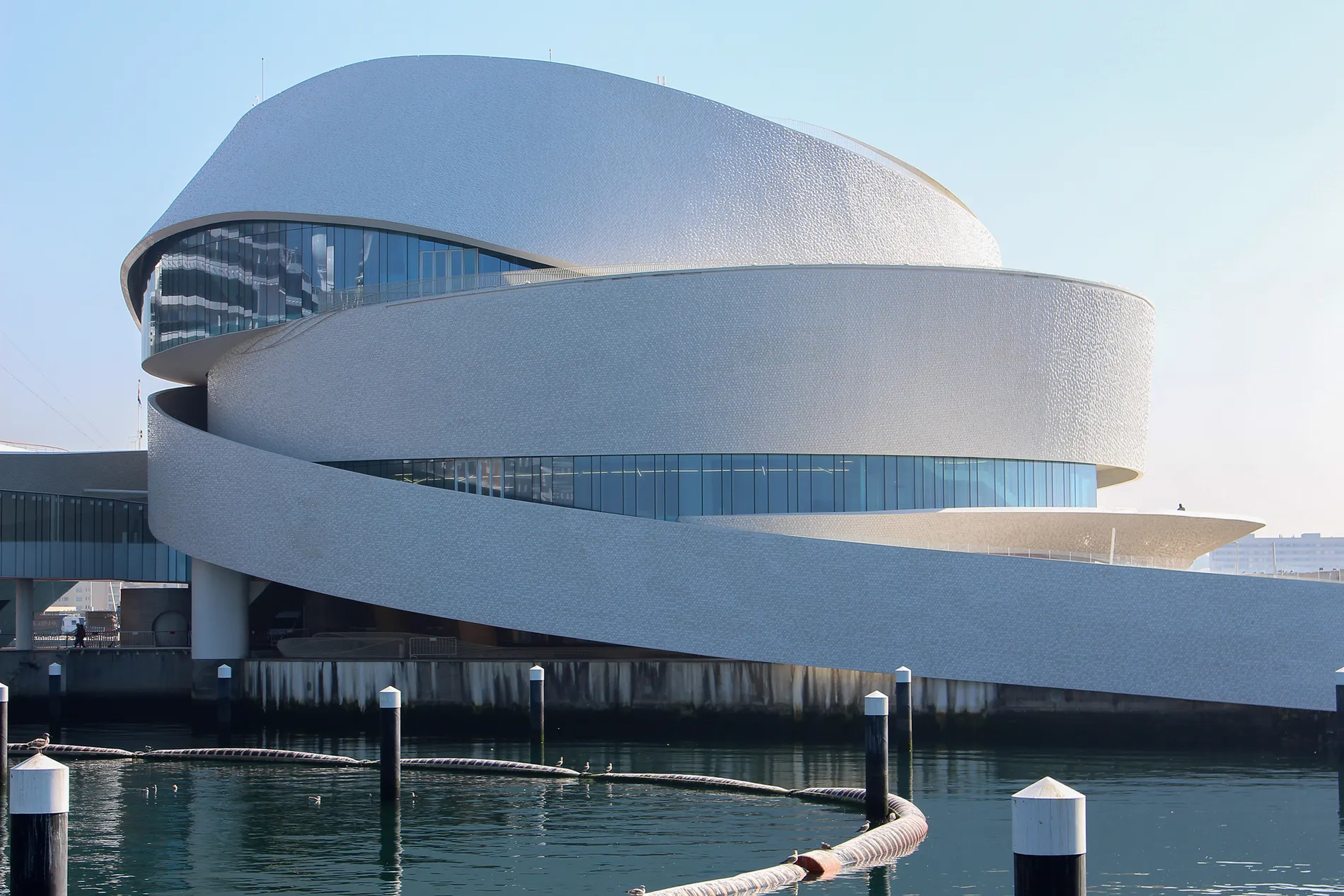 A modern, spiral-shaped building by the water with a reflective glass facade.