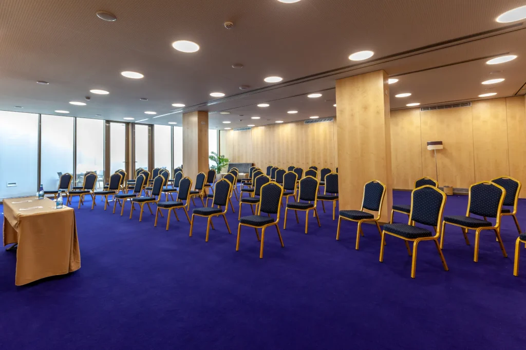 Empty conference room with blue chairs arranged in rows on a purple carpet.