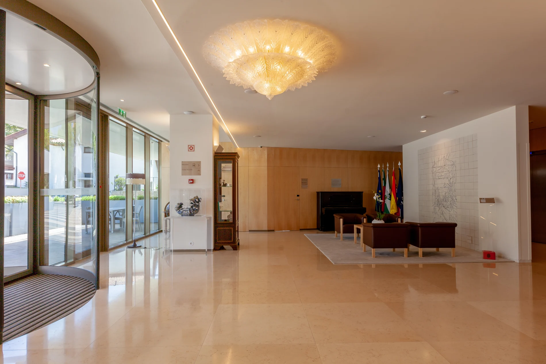 Elegant lobby with a plush sofa, flags, and a chandelier, next to glass entrance doors.