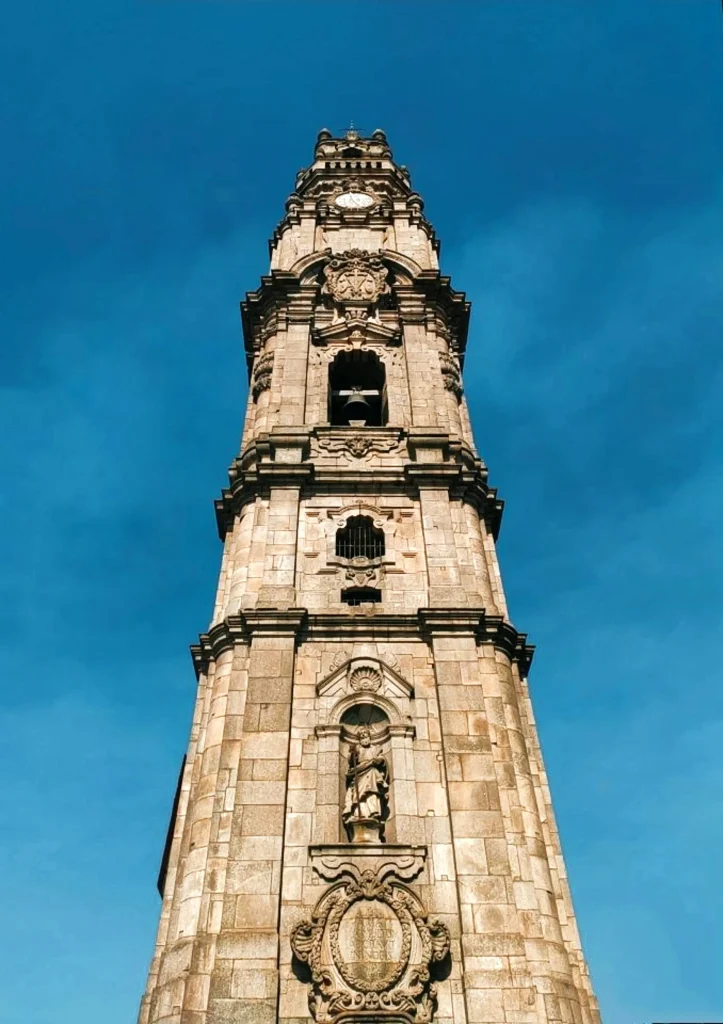 Tall stone tower with clock and statue details under a clear blue sky.