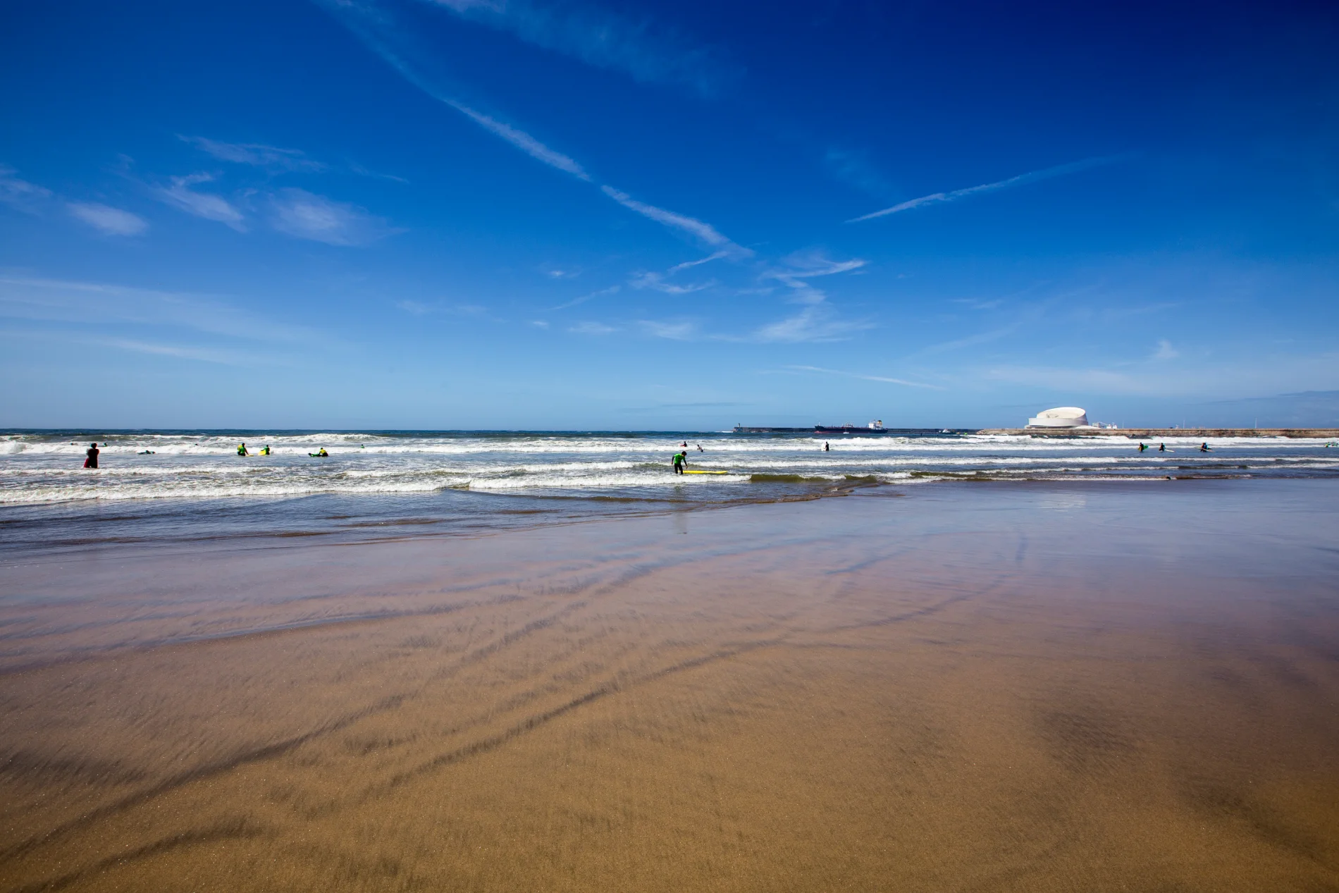 Beach scene with people in the water under a clear blue sky.