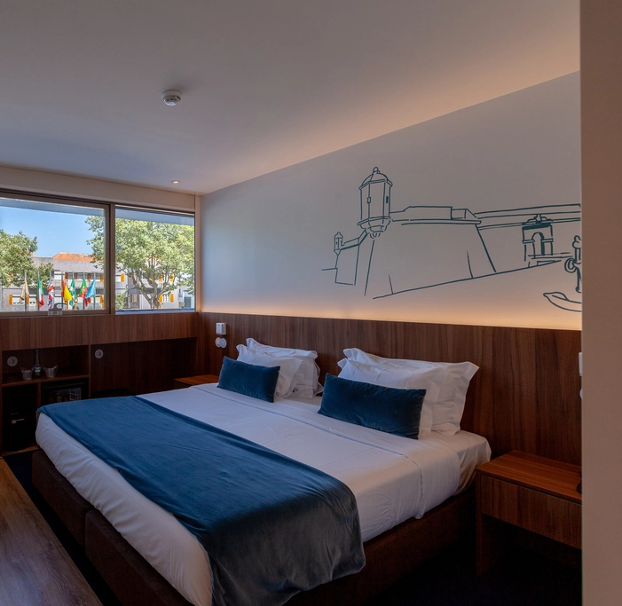 Hotel room with large bed, wall art, and window view of flags and trees.