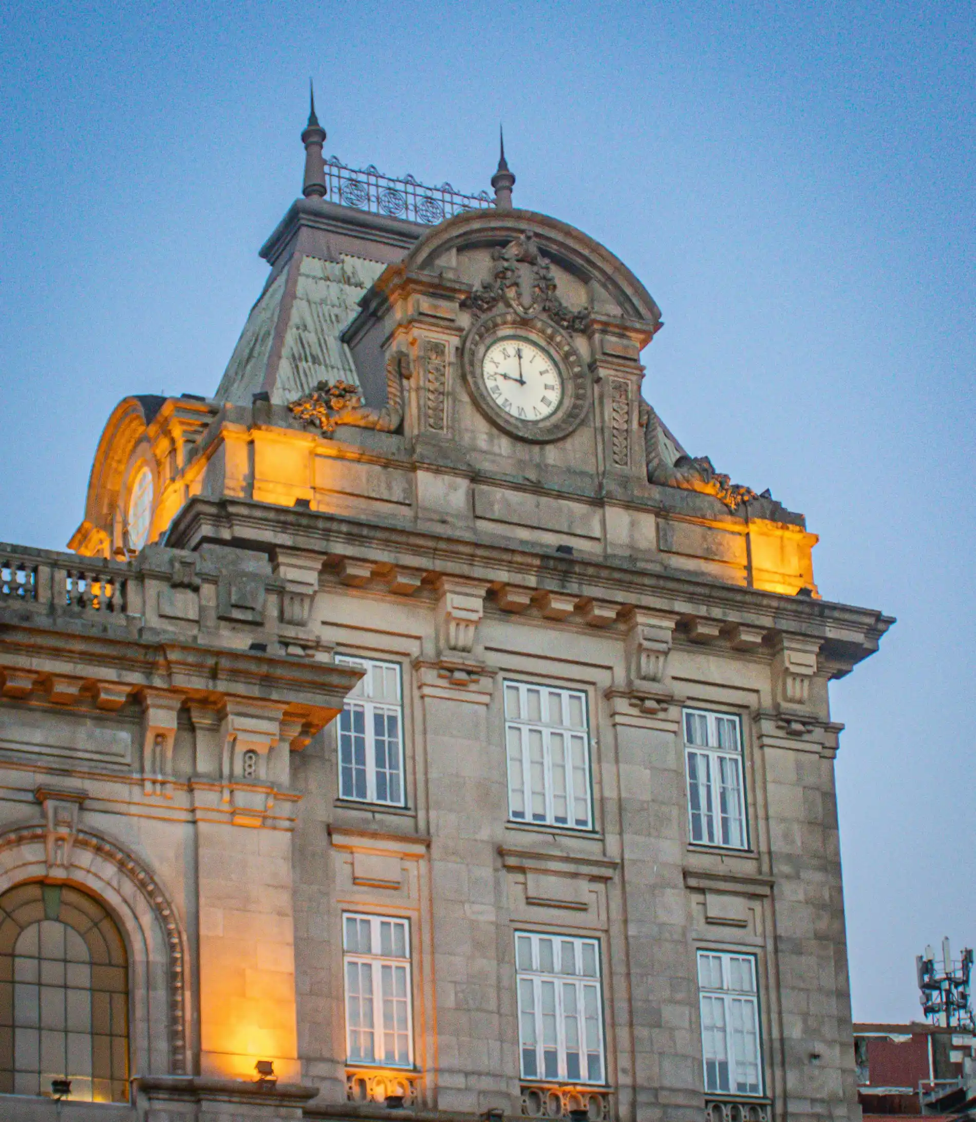 Historic building facade with a large clock and warm lighting, set against a clear sky.