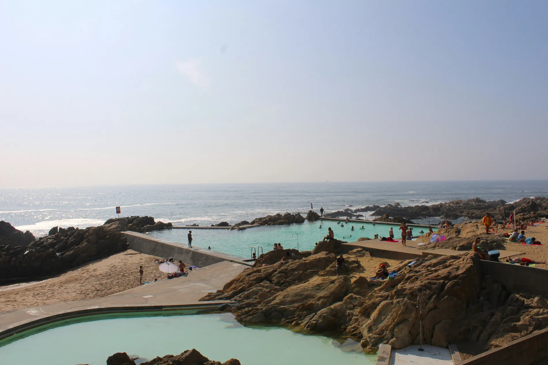 Rocky beach with people swimming in a tidal pool under a clear sky.