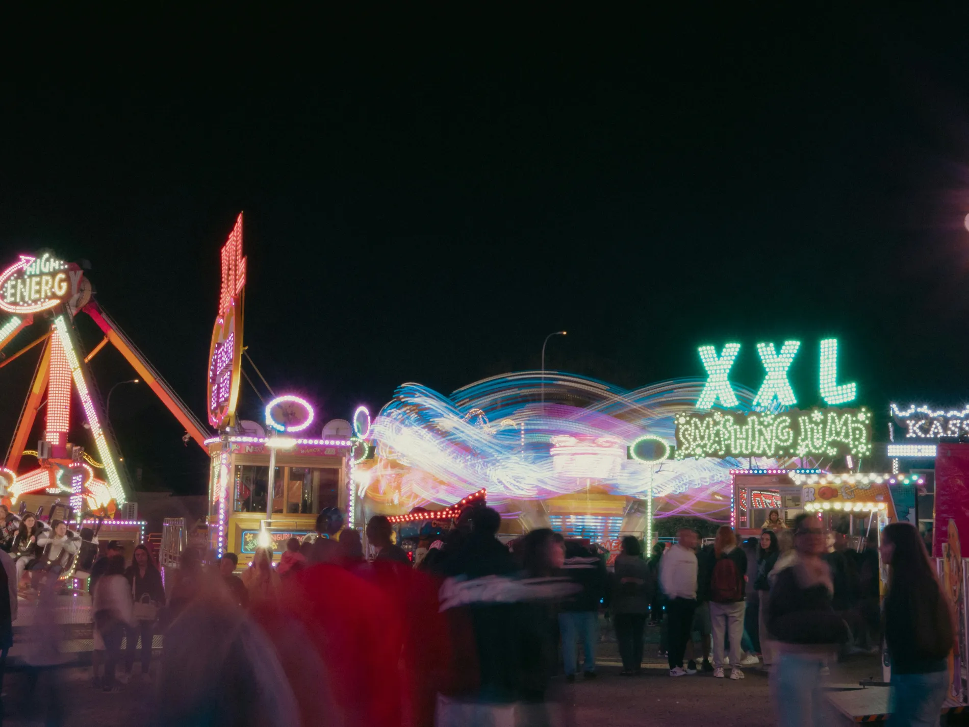 People at a colorful night carnival with rides and neon lights.