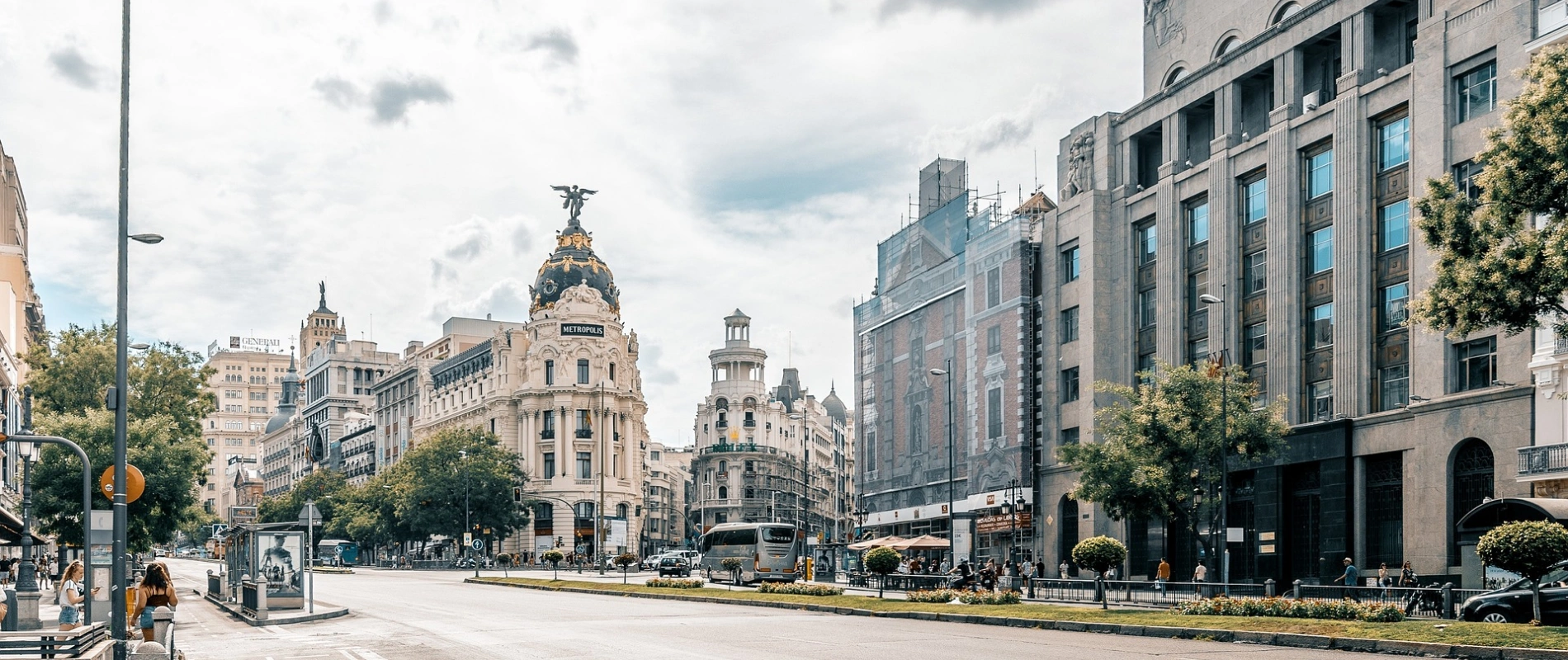 Calle con edificios históricos y árboles; personas caminando y autos circulando.